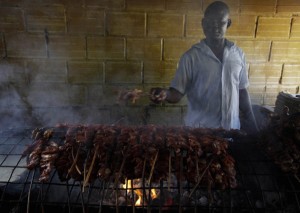 In this photo taken on Saturday, Oct. 20, 2012, a man grills meat to make suya in Lagos, Nigeria. As night falls across Nigeria, men fan the flames of charcoal grills by candlelight or under naked light bulbs, the smoke rising in the air with the smell of spices and cooking meat. Despite the sometimes intense diversity of faith and ethnicity in this nation of 160 million people, that thinly sliced meat called suya, is eaten everywhere. (AP Photo/Sunday Alamba)